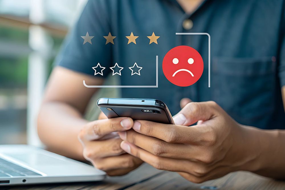 Foto: Mann bedient Smartphone, darüber negatives Smiley und schlechte Sterne Bewertung